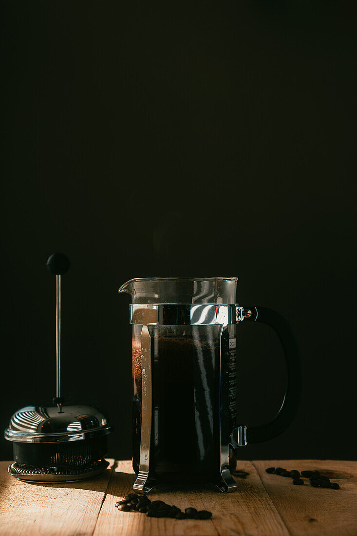 Kaffeekanne mit frisch gerösteten Bohnen, serviert auf einem Holztisch vor schwarzem Hintergrund