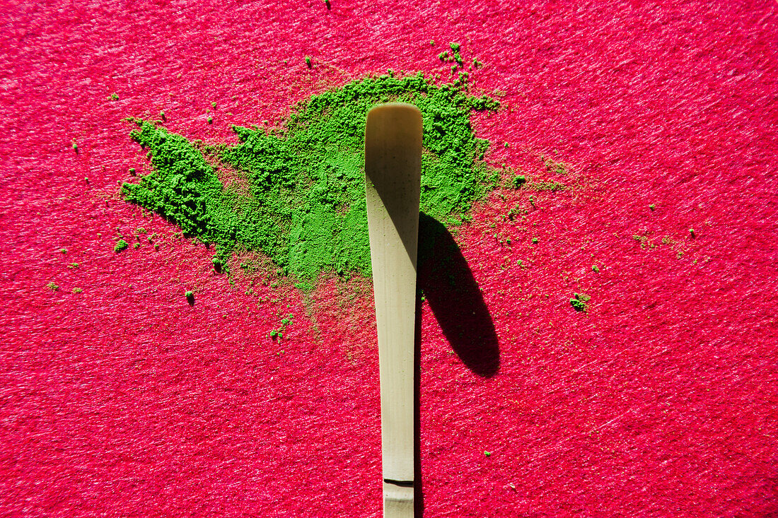 Top view of bamboo chashaku and scattered green Japanese matcha tea on bright pink surface at sunlight