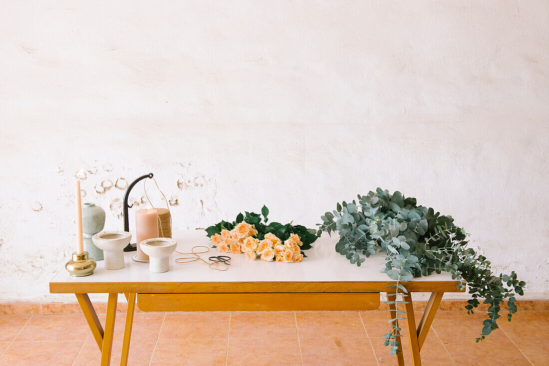 Strauß frischer duftender Rosen und Eukalyptusblätter auf dem Tisch neben Kerzenvasen und Jutefadenspule im Blumenatelier