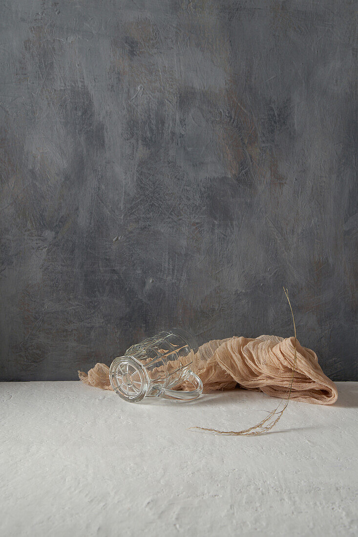 Glass cup and cloth placed with tree twig on beige and gray background