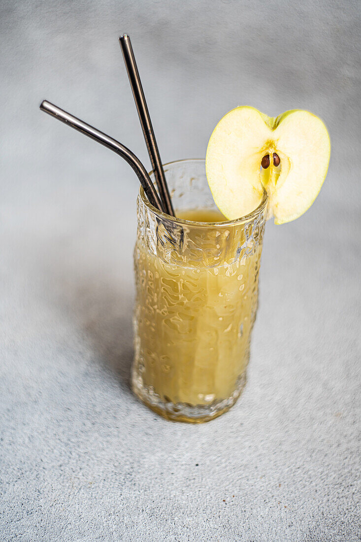 Fresh apple smoothie served in glass with sliced apple on concrete background