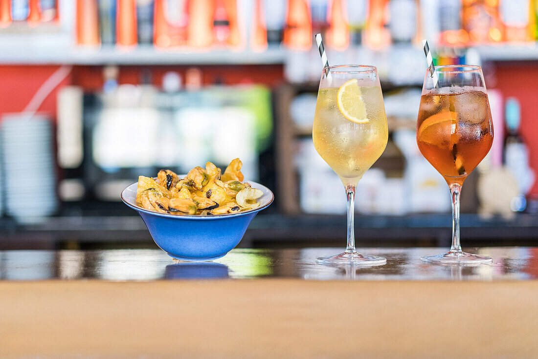 Bowl with tasty seafood appetizers and glasses of cold fresh cocktails served on wooden counter in bar