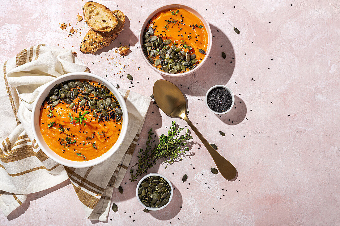 Top view of appetizing homemade pumpkin purees with seeds and herbs in bowls placed on table near crispy bread slices in kitchen