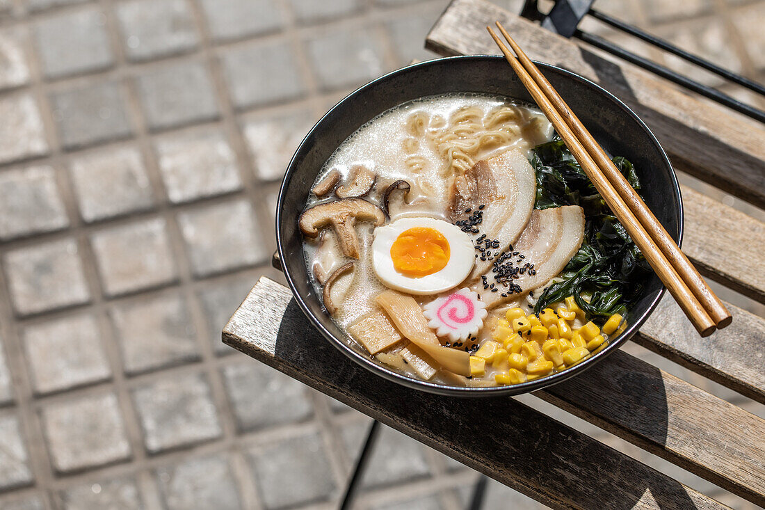 Von oben der appetitlichen japanischen Ramen mit Pilzen und Ei auf Schüssel auf Ecke des Tisches auf der Terrasse des Restaurants auf sonnigen Straße in der Stadt serviert