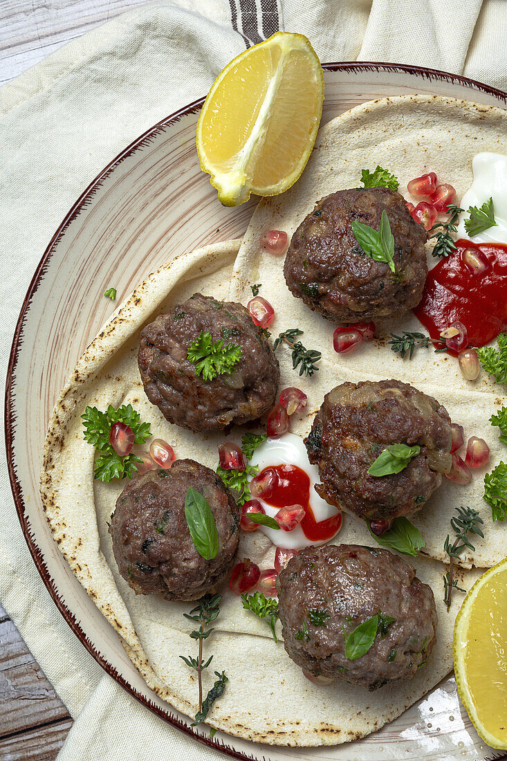 Traditional homemade beef and lamb meatballs with arabic bread, tomato sauce, pomegranate and aromatic herbs. Halal food