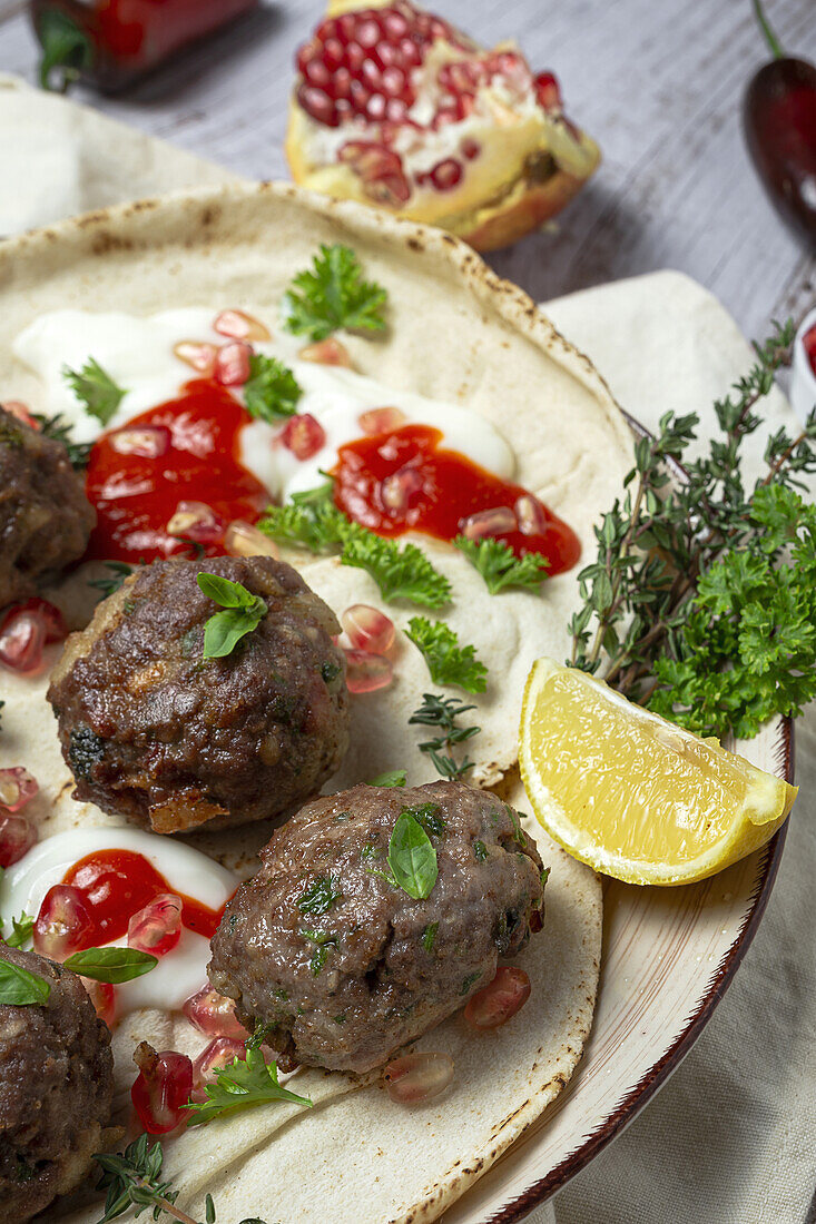 Traditional homemade beef and lamb meatballs with arabic bread, tomato sauce, pomegranate and aromatic herbs. Halal food