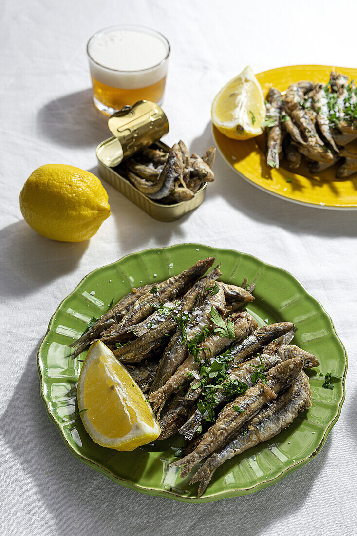 From above of delicious fried anchovies served on plates with lemon and placed on white table with glass of beer
