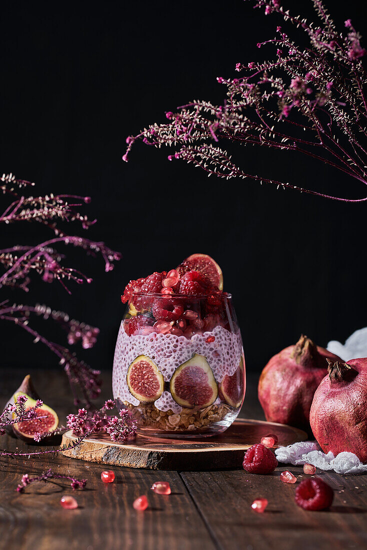 Side view of fresh fruit jam in small jar with full and cut figs on plate at black kitchen table next to pomegranates