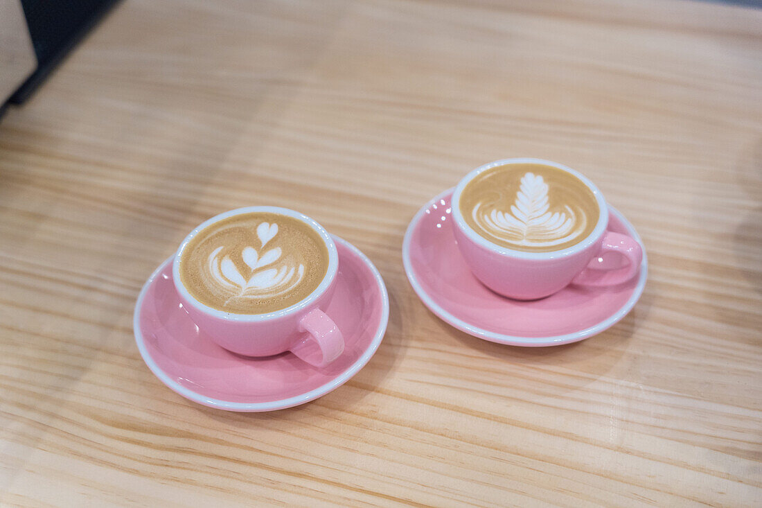 Becher mit heißem Kaffee mit kreativer Latte Art auf Teller mit Teelöffel auf Holztisch in modernem hellen Kaffeehaus serviert