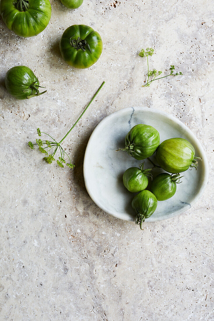 Top view of green fresh tomatoes and dill sprig placed on marble plate on table