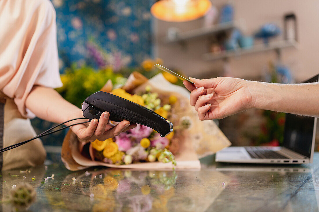 Nicht erkennbare Kundin, die eine Plastikkarte benutzt und am POS-Terminal für eine Bestellung in einem Blumenladen bezahlt