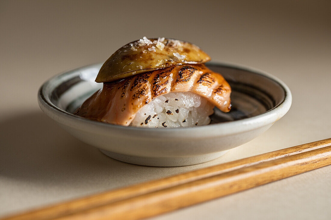 Leckere japanische Nigiri-Sushi mit geräuchertem Lachs und flambierter Gänsestopfleber, serviert auf einem Teller mit Stäbchen im Restaurant