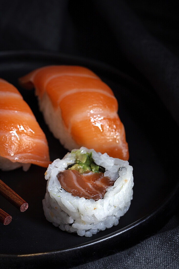 Top view composition of delicious fresh sushi and bamboo chopsticks served on black platter on checkered cloth