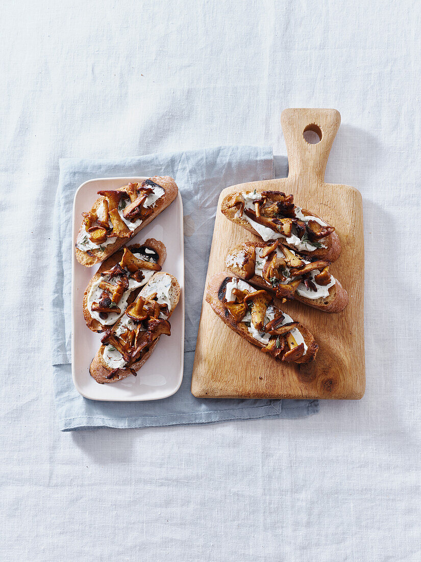 Bruschetta mit Pfifferlingen und Frischkäse, serviert auf einem kleinen Holzschneidebrett