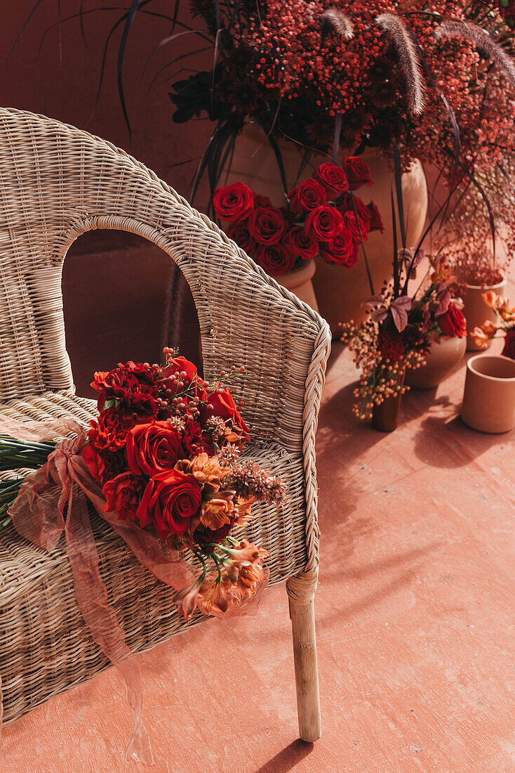 Fresh red flowers in bouquet tied with thin ribbon placed on wicker chair at sunshine