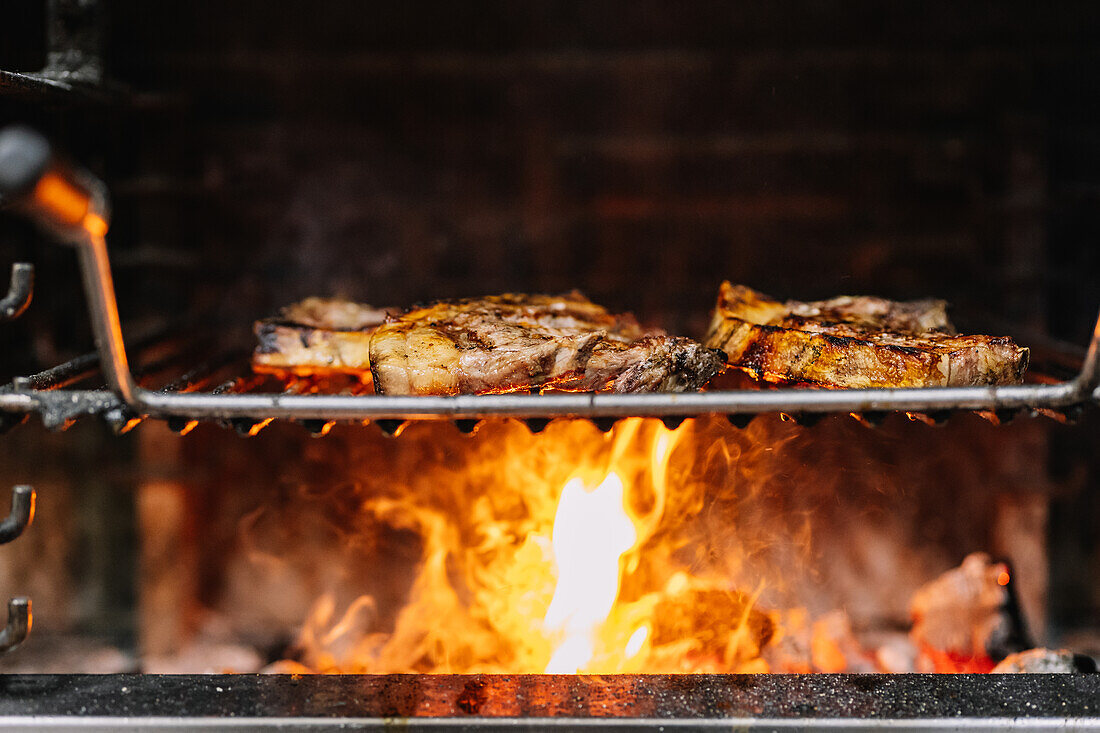 Appetizing juicy steaks placed on barbecue grid over burning flame while frying in grill oven