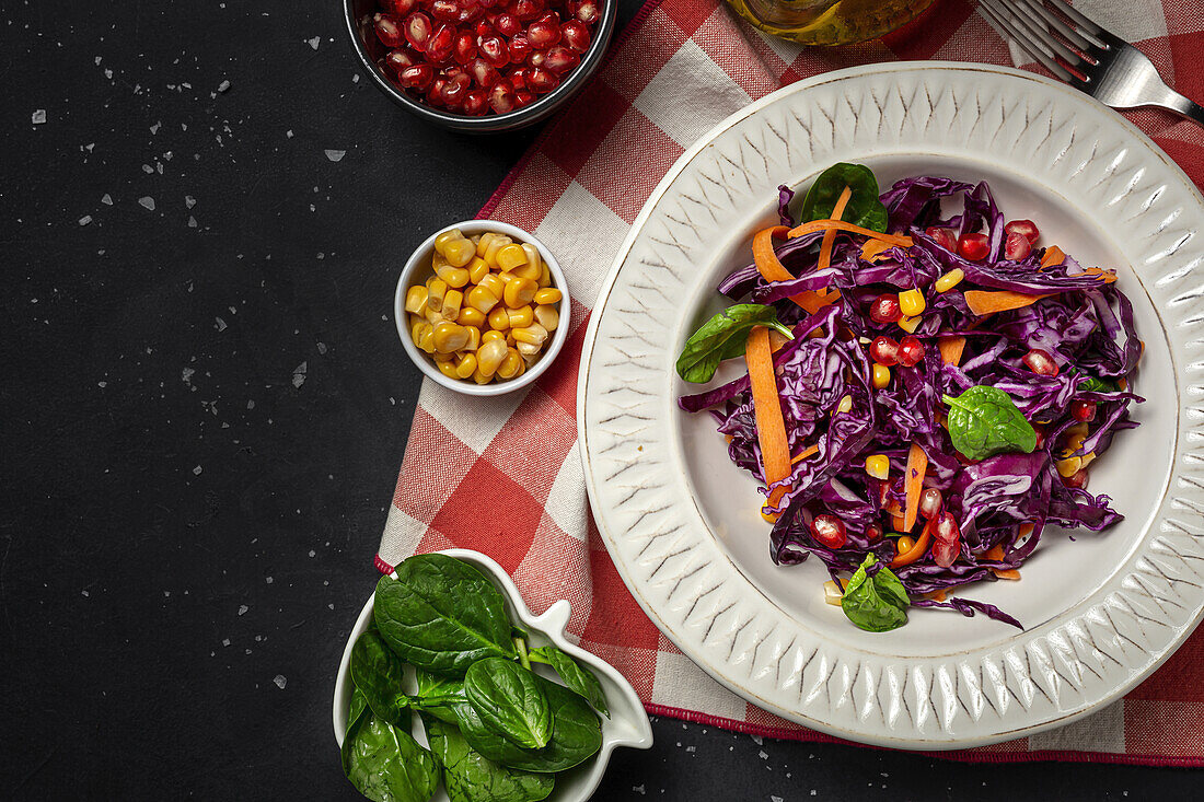 Hausgemachter lila Krautsalat mit Mais, Karotten, Granatapfel und Spinat auf dunklem Hintergrund. Vegane Ernährung Konzept. Gesundes Essen