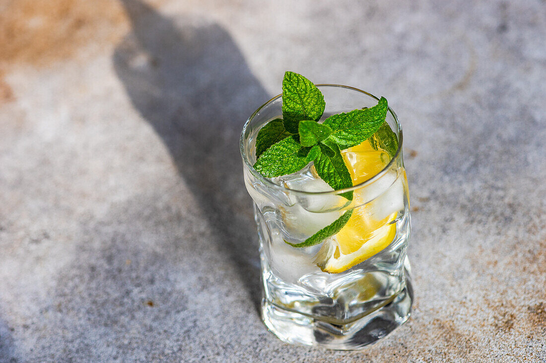 Glass of lemon water with mint on concrete background in sunny day with shadows