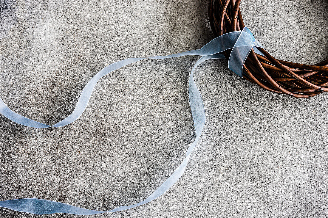 From above grape vine wreath decorated with pale blue ribbon on grey concrete background