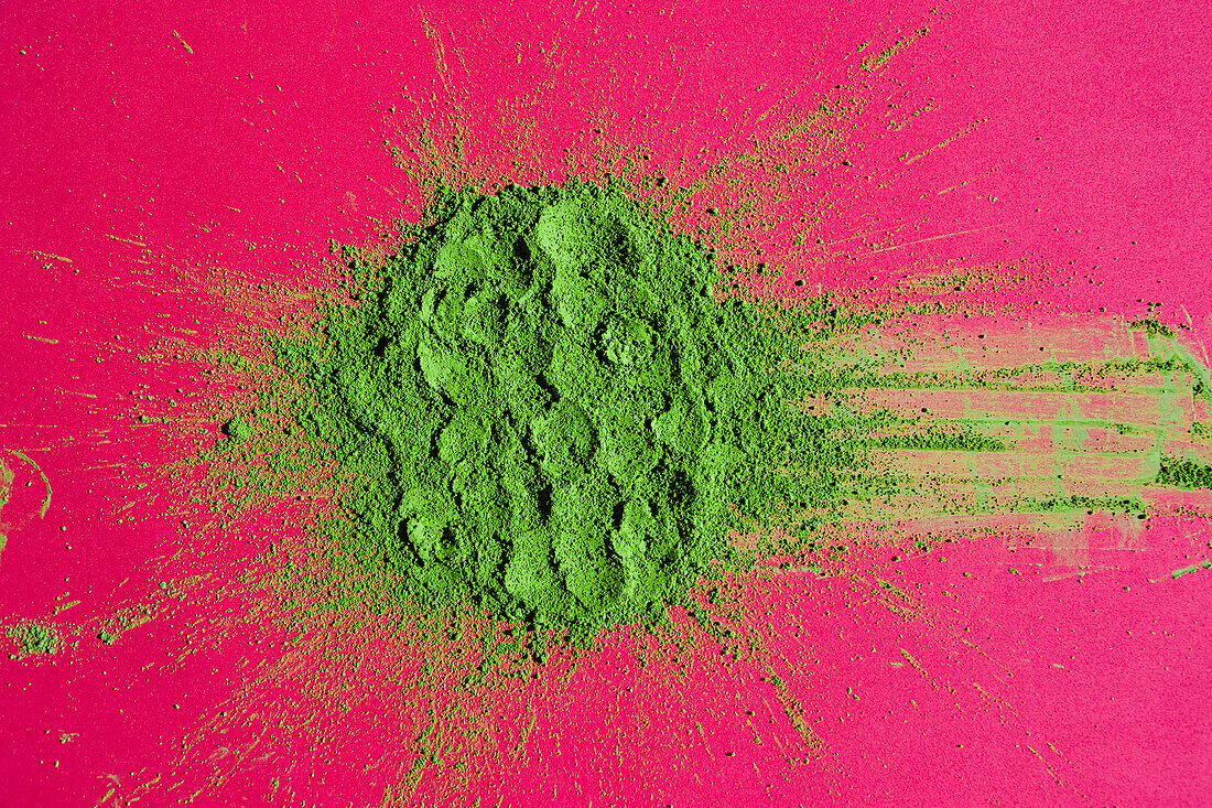 Top view of traditional Japanese powdered matcha tea scattered on bright pink background