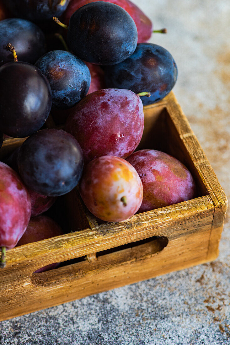 Fresh organic and ripe plum fruits in wooden box on concrete background