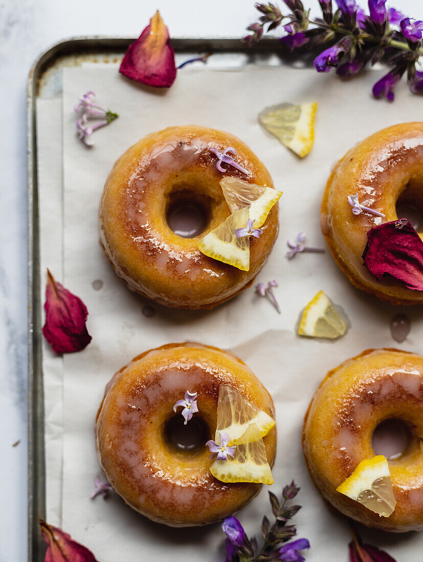 Draufsicht auf leckere Donuts auf Kühlregal mit Blättern zwischen blühenden Lavendelzweigen auf Marmoroberfläche