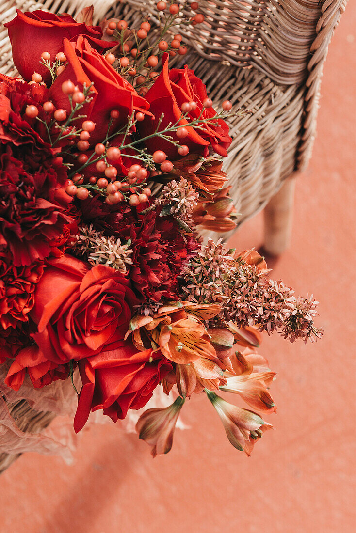 High angle of fresh red flowers in bouquet placed on wicker chair at sunshine