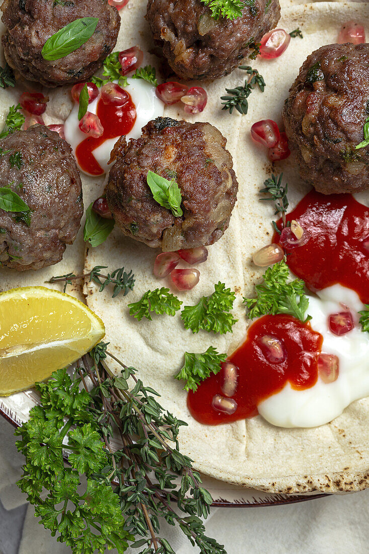 Traditional homemade beef and lamb meatballs with arabic bread, tomato sauce, pomegranate and aromatic herbs. Halal food