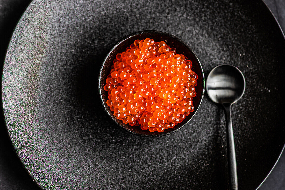 From above red fresh trout fish caviar served in a bowl on concrete table background