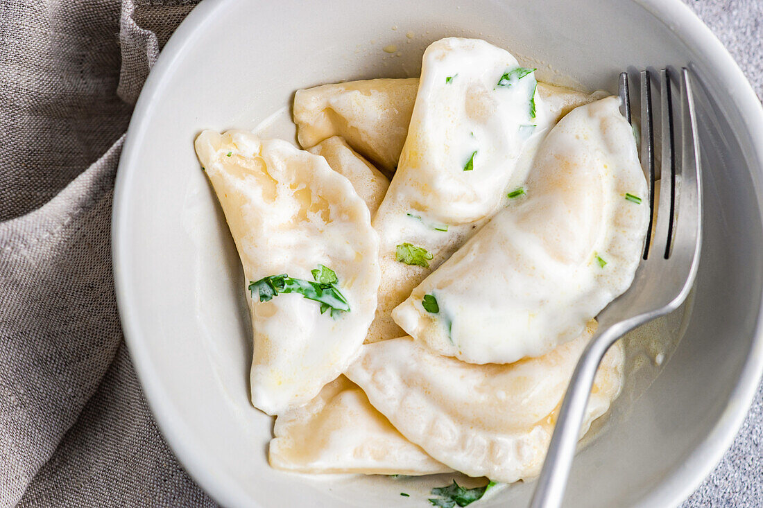 Von oben traditionelle ukrainische Knödel mit Kartoffelfüllung, die bekannten Vareniki, serviert in einer Schale mit saurer Sahne