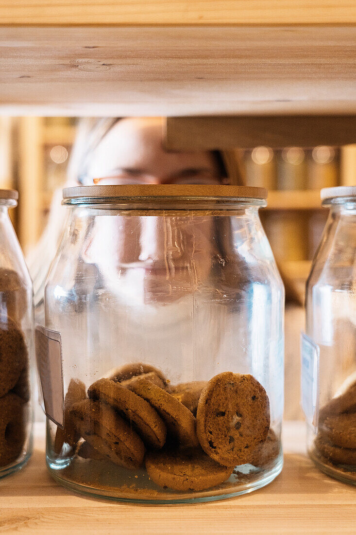 Set of glass jars with chocolate cookies placed on wooden shelf in shop