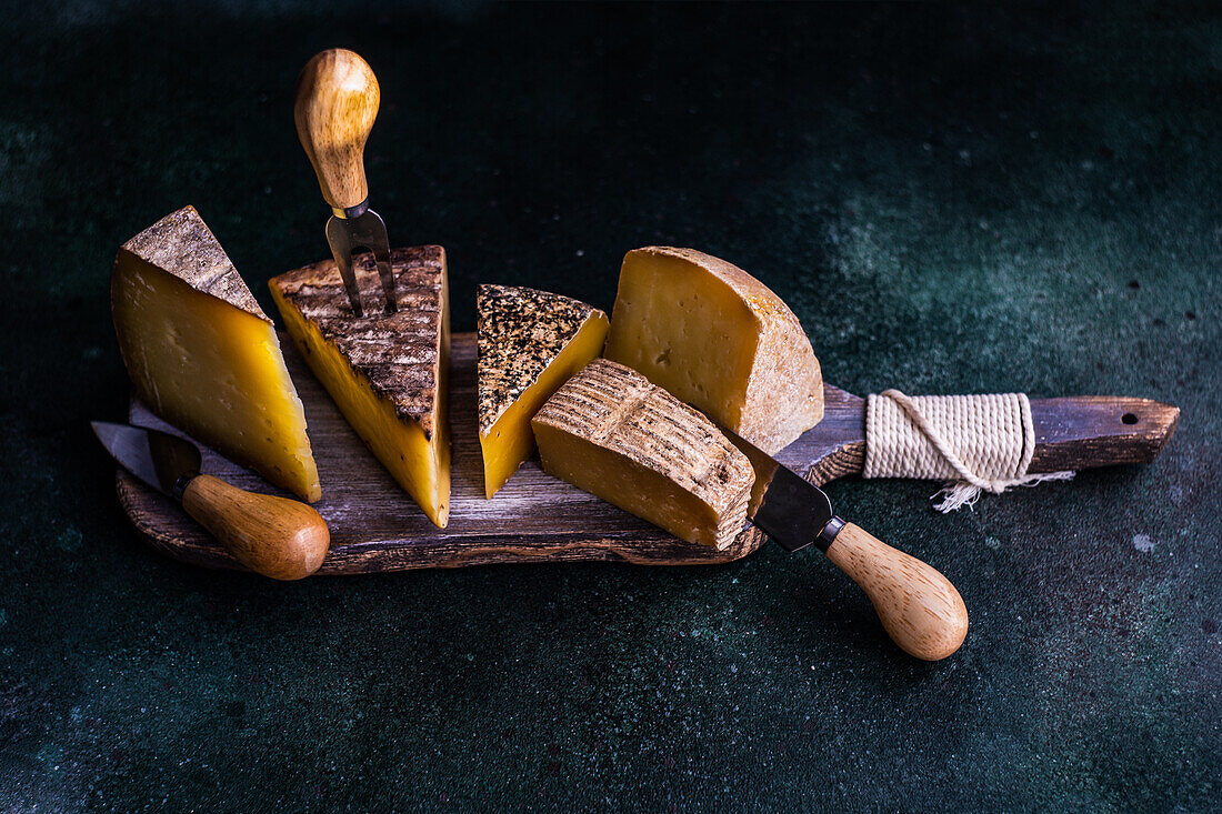 Wooden cutting board with cheese variety on dark concrete background