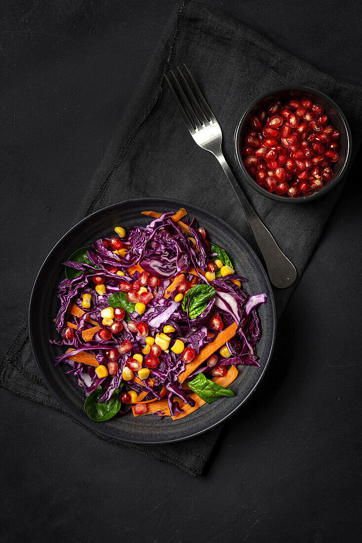Homemade Purple Cabbage Salad with Corn, Carrots, Pomegranate and Spinach on dark background. Vegan food concept. Healthy food