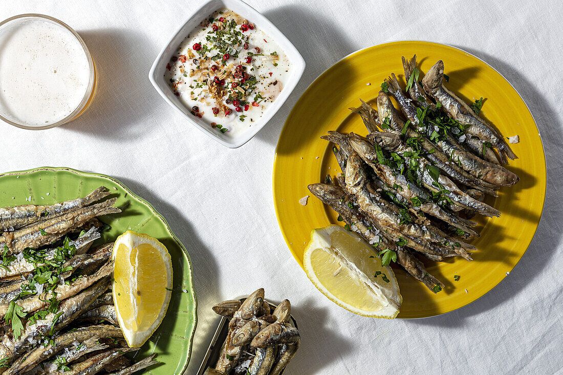 From above of traditional Spanish fried boquerones served on plates with lemons and bowl of white soup placed on table with glass of beer in restaurant