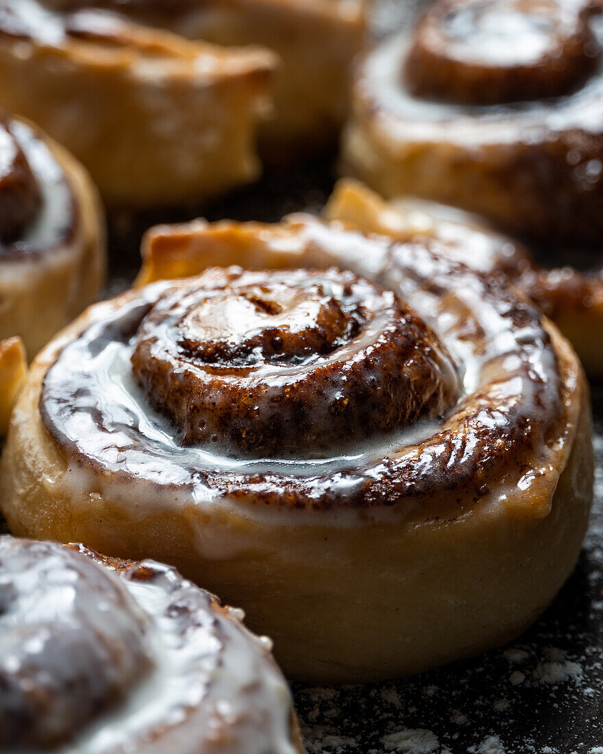 Appetizing baked sweet cinnamon rolls with white cream topping served on table in bakery