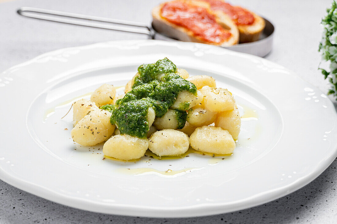 Appetizing gnocchi with pesto sauce served on white plate with toasts