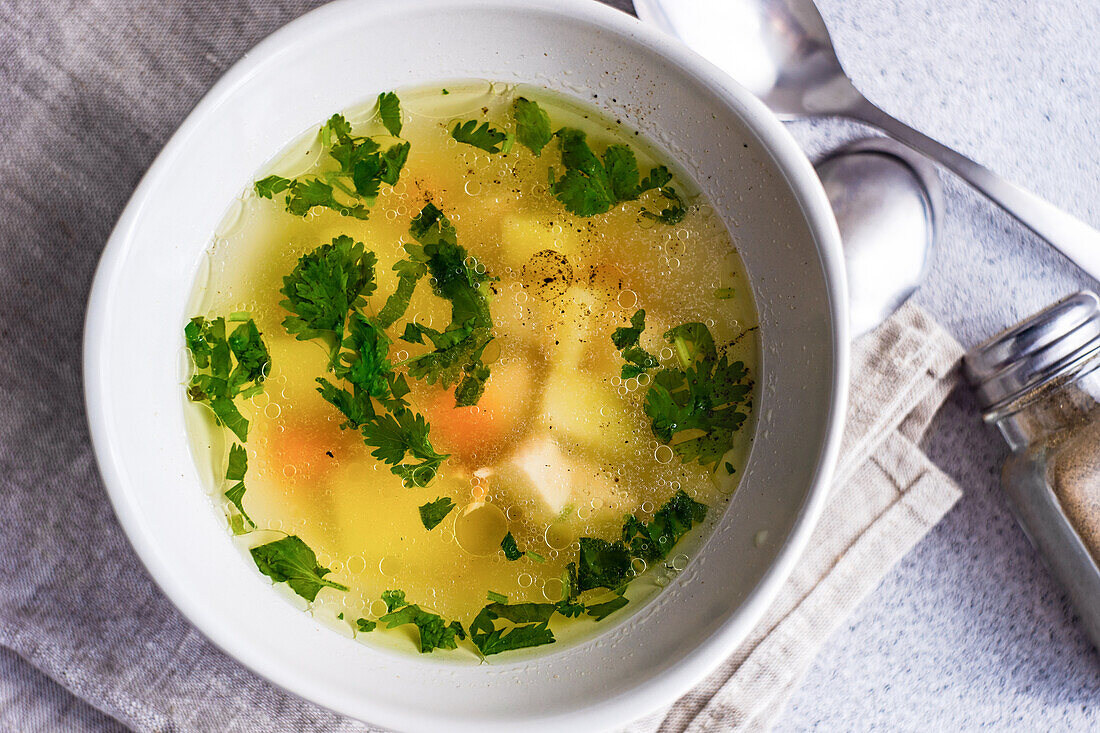 Von oben: Hühnersuppe mit Gemüse in Schalen auf weißem Betontisch, bereit zum Abendessen