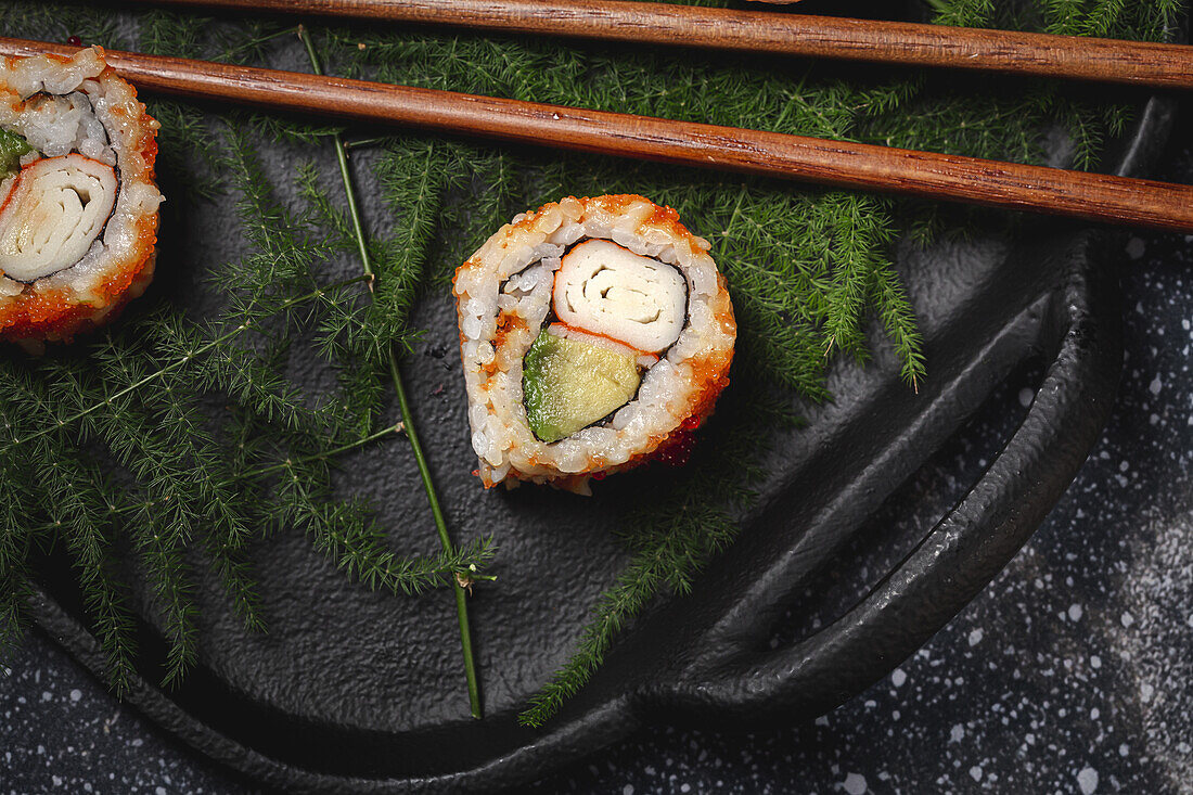 Top view Komposition von köstlichen frischen verschiedenen Sushi und Bambus-Essstäbchen auf schwarzem Teller auf karierten Tuch serviert