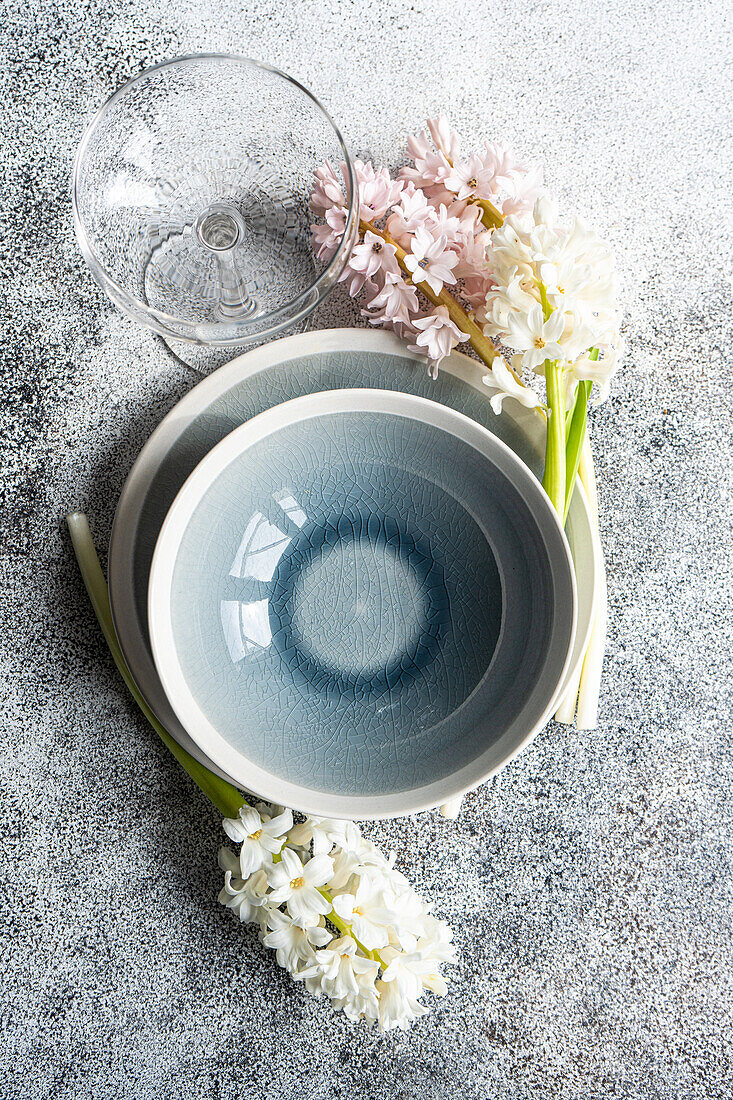 Frühlingshafte Tischdekoration mit Hyazinthenblüten neben Keramiktellern und Besteck auf einem grauen Betontisch für ein festliches Abendessen