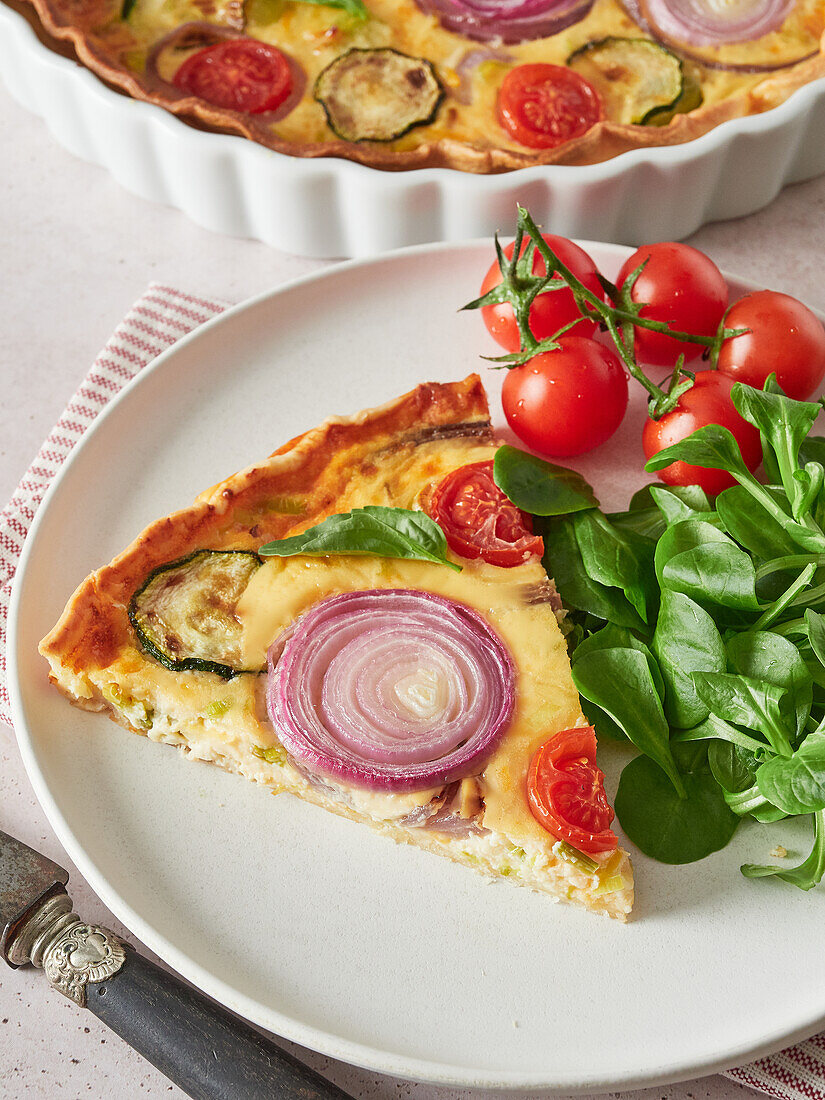 High angle of tasty vegetable quiche served on plate with ripe cherry tomatoes and fresh basil spinach during lunch at home