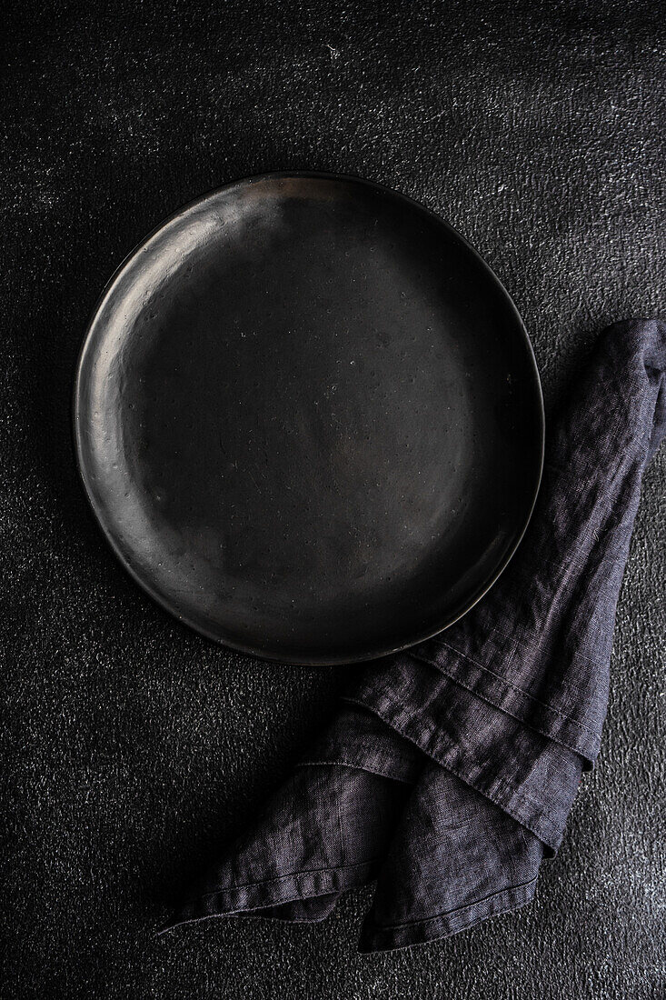 From above minimalistic table setting with black ceramic plate on the same color concrete background