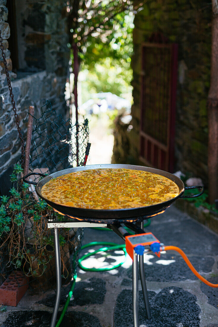 Large iron pan with steaming ingredients placed on fire during preparation of traditional Spanish paella in garden