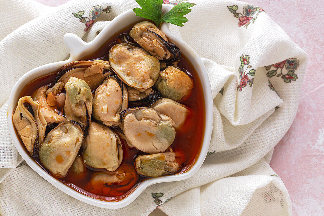 From above ceramic plate with yummy mussels in sauce standing on piece of cloth on gray background