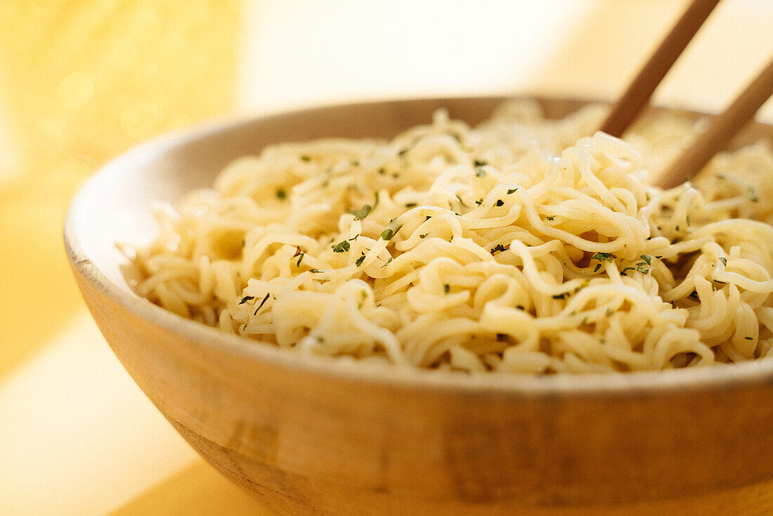 Nahaufnahme einer Schüssel mit köstlichen Nudeln mit Gewürzen auf gelbem Hintergrund mit hölzernen Stäbchen in einem hellen Raum