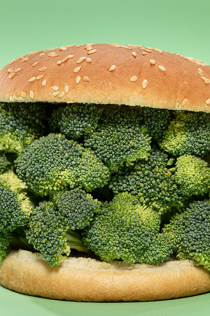 Hälften eines Burgerbrötchens mit einem Bündel roher Brokkoli auf grünem Hintergrund während eines gesunden Mittagessens