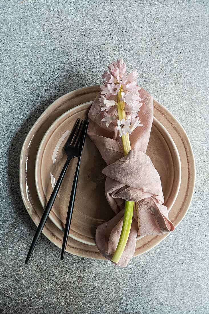 Frühlingshafte Tischdekoration mit Hyazinthenblüten neben Keramiktellern und Besteck auf einem grauen Betontisch für ein festliches Abendessen