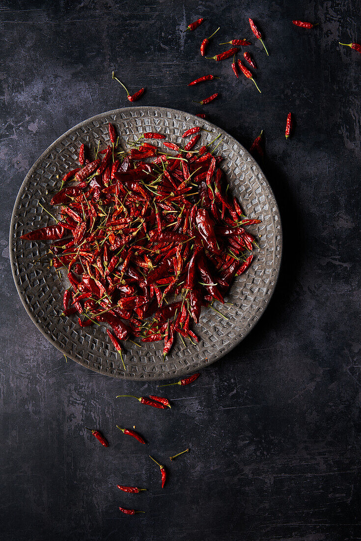 Top view of pile of dried red hot chili peppers placed on plate and scattered on gray marble table