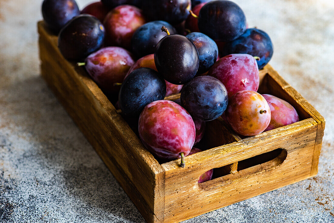 Fresh organic and ripe plum fruits in wooden box on concrete background