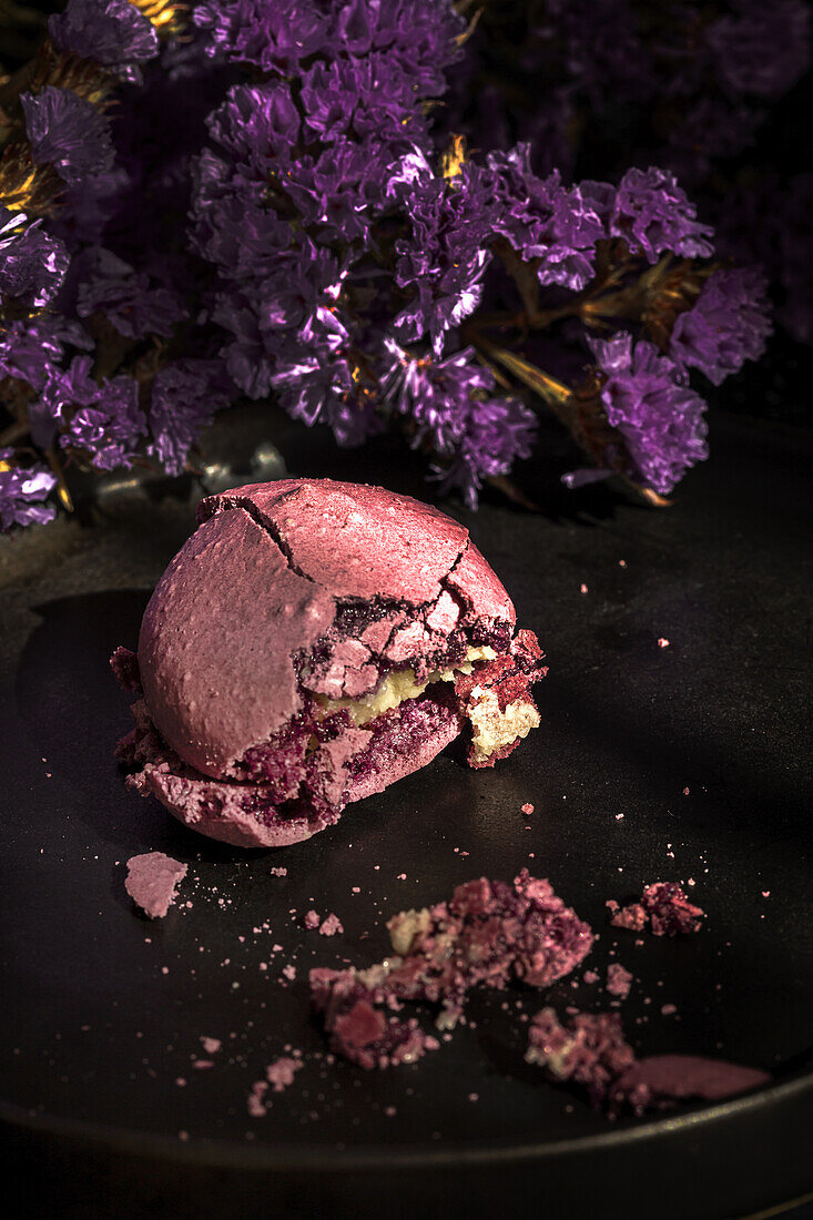 From above bouquet of fresh violet flowers placed on marble table near plate with crushed macaroon in morning.