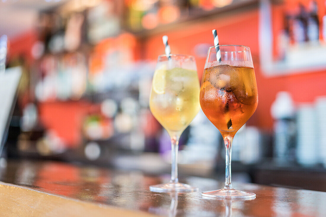Glasses of cold fresh cocktails served on glass with straw on wooden counter in bar
